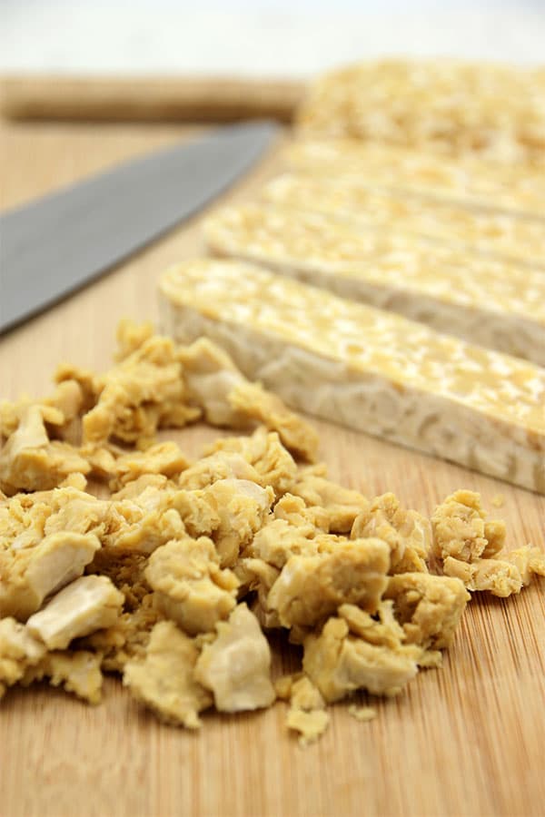 Crumbled and sliced tempeh on chopping board with knife