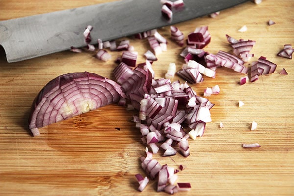 diced red onion on wooden board with knife
