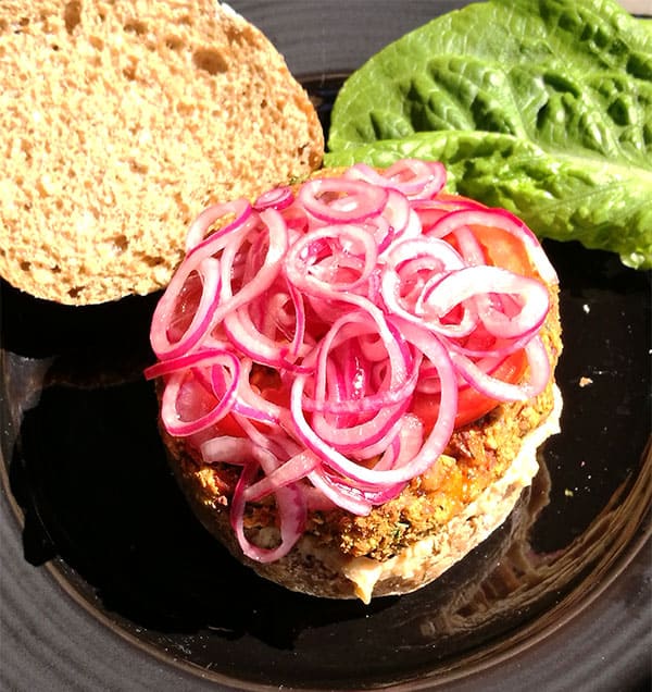 Mediterranean veggie burgers are topped with pickled red onions on a bun with a black plate.