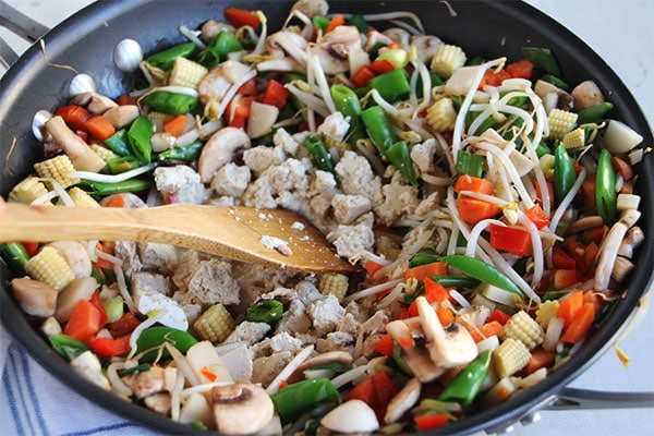 tofu is being added to mixed vegetables in black wok.