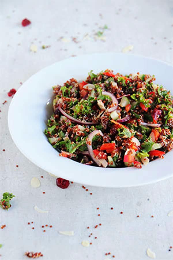cranberry quinoa salad in white bowl on white board with dried cranberries, almonds and quinoa