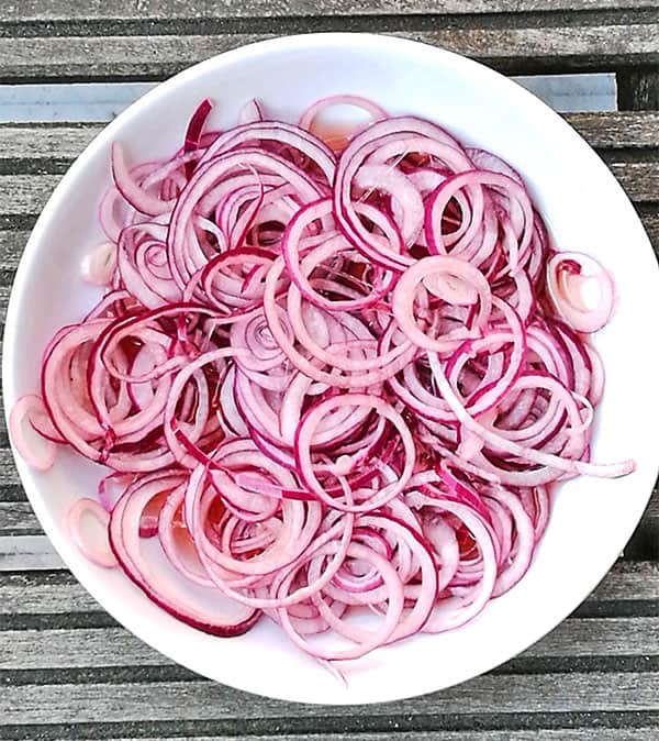 red onion slices in white bowl with red vinegar marinade in bottom of bowl.