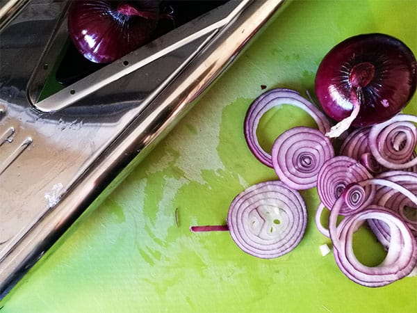 red onions slices on bright lime green board with mandolin in background.
