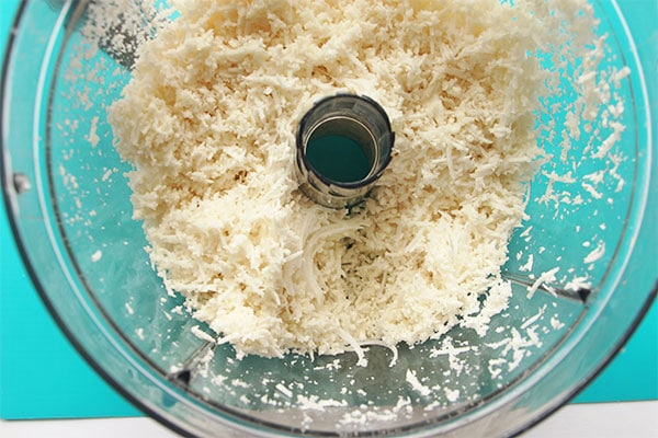 A food process is filled with grated cauliflower on a blue mat.