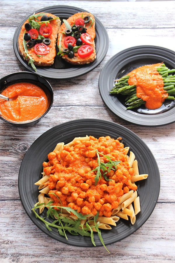 Red pepper Romesco sauce over chickpeas, over asparagus, and bruschetta with sauce in black bowl.