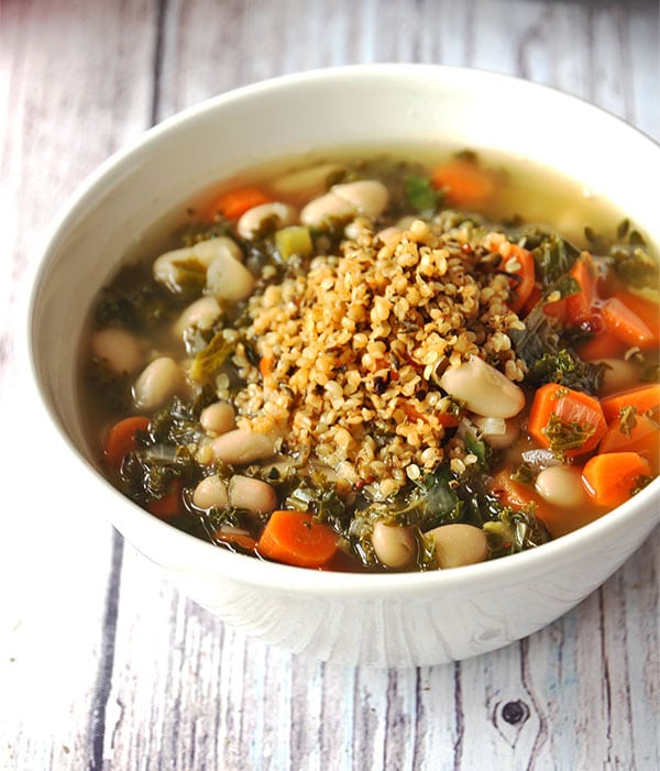 Italian white bean soup with carrots and kale in single white bowl topped with hemp seed Parmesan.