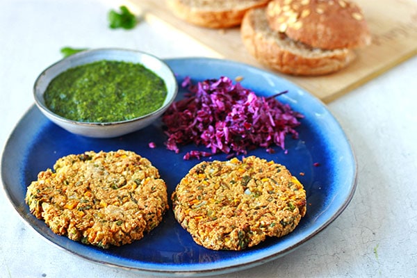 2 baked samosa burger patties on blue plate with red cabbage and coriander mint sauce in small bowl
