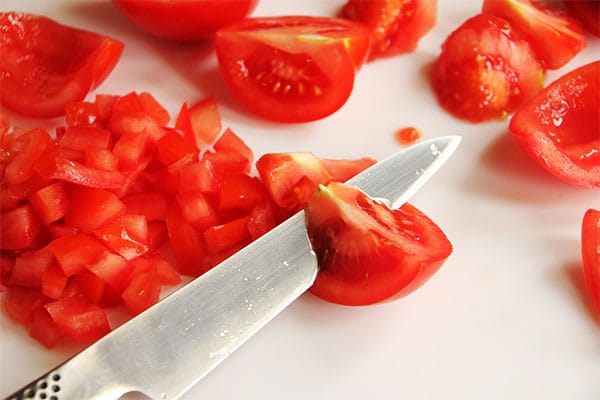 knife is used to cut the core and seeds from tomatoes on white cutting board.