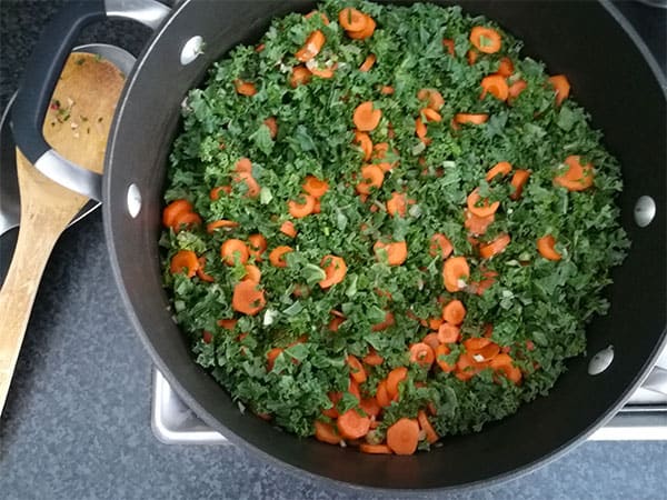 sliced carrots and kale in black soup pot on stove top.