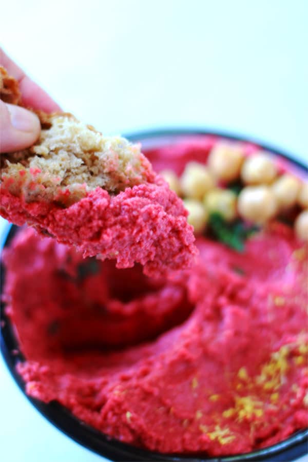 dipping bread into bowl of red spicy beetroot (oil free) hummus.