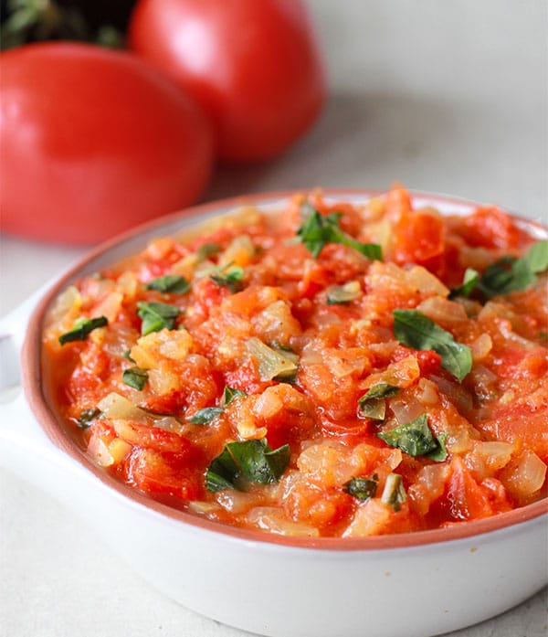 tomato chutney in small white dish with fresh tomatoes in background.