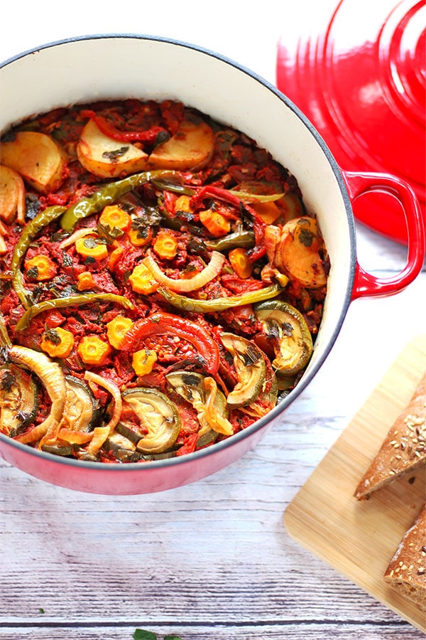 Red casserole dish filled with roasted vegetables (potatoes, green peppers, onions, carrots, zucchini and tomatoes, with chopped parsley.