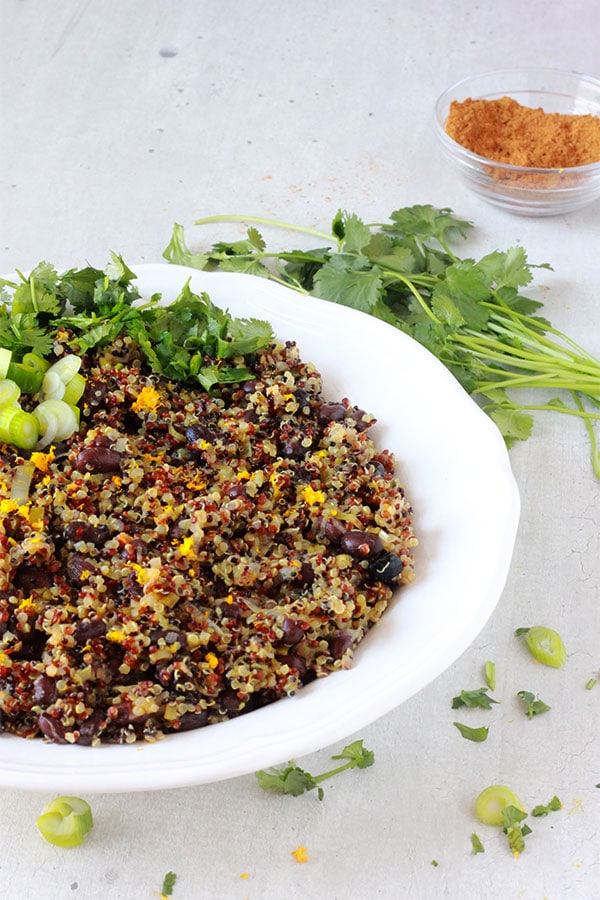 orange quinoa black bean pilaf in large white bowl with fresh coriander and Berbere spice blend.