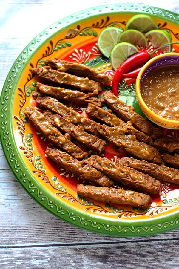 soy strips with satay sauce on green and yellow plate with bowl of sauce in middle.