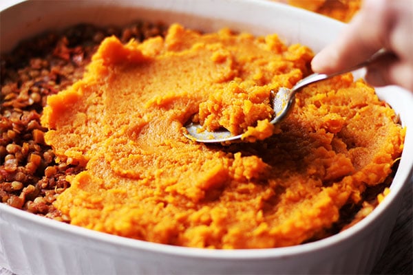 spreading sweet potatoes with spoon over red lentil filling