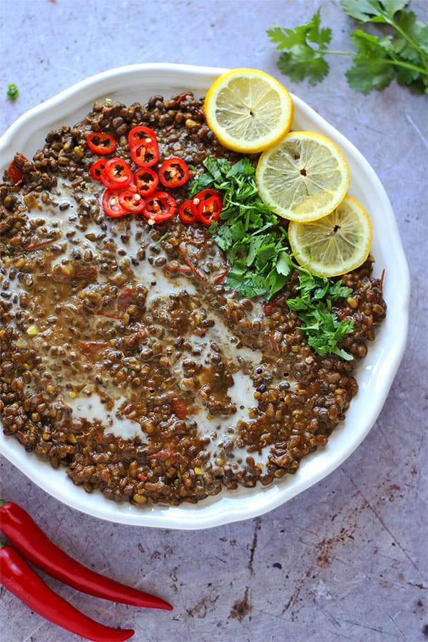 Dal Makhani - black lentil dal in white bowl garnished with sliced red chilis, lemon slices and cilantro with red chili peppers and cilantro on stone board.
