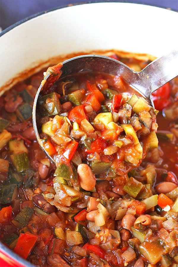 close up of red soup pot with zucchini, red pepper, berlotti bean chili with ladle filled with chili.