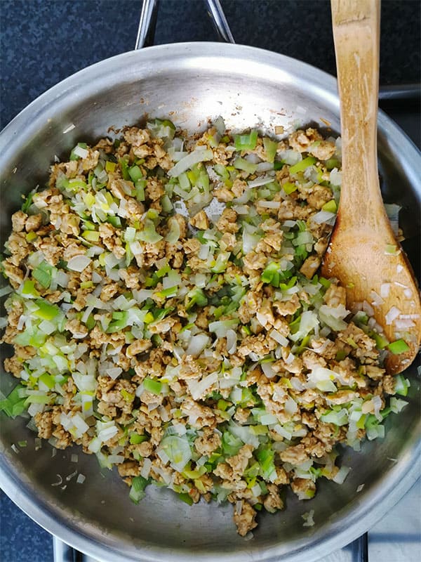 Tempeh is crumbled and added to stainless steel pan with chopped leeks and onions and sauteed.
