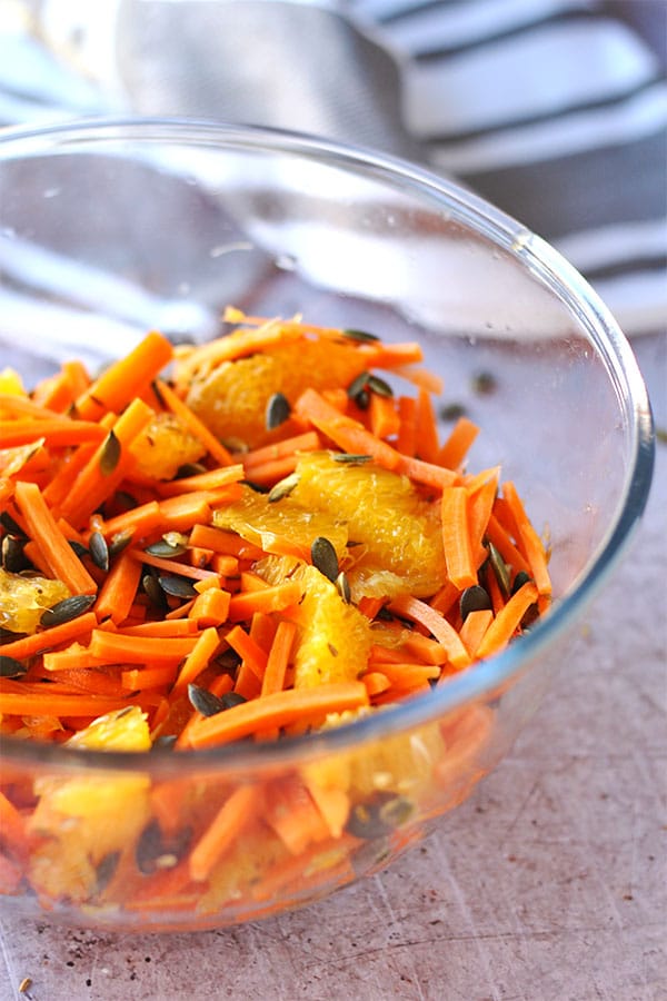 carrot orange cumin slaw with pepitas and cider vinegar in glass bowl