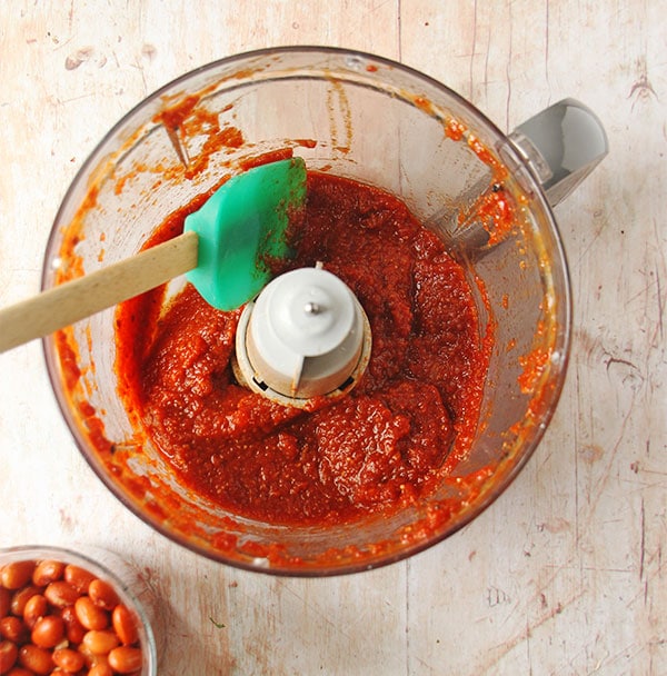 Overhead shot of red chili sauce in blender with small dish of beans beside it.