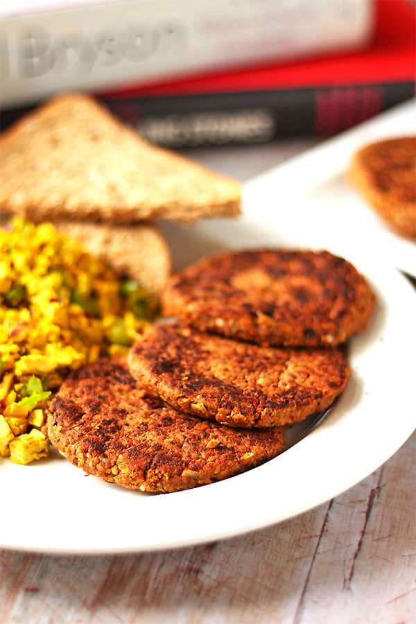 tempeh breakfast sausage patties on round white plate with scrambled tofu and green pepper.