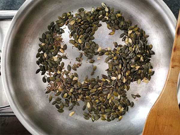 toasted cumin seeds and pepitas (pumpkin seeds) in stainless steel pan.