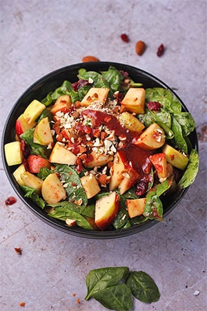 Overhead shot of apple cranberry salad with spinach and chopped almonds in black bowl.