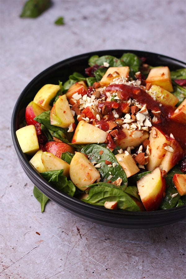 apple cranberry salad with spinach, chopped almonds, diced apples and cranberry dressing in black bow.