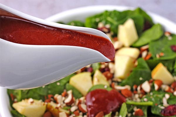 Salad dressing made with cranberries and balsamic vinegar is poured over salad.