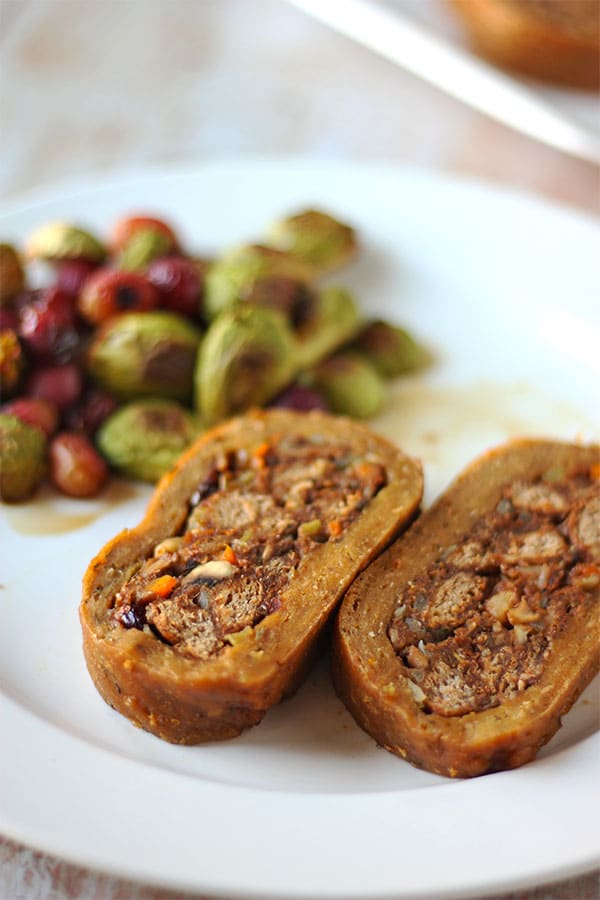 Slices of stuffed seitan roast on white plate with Brussel's sprouts in background.