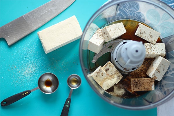 tofu is diced and added to a food processor with tamari, garlic and onion powder, maple syrup, liquid smoke and black pepper.