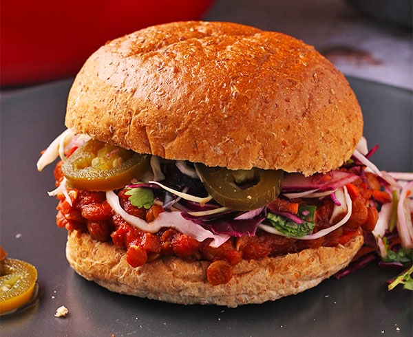 Vegan lentil sloppy joes with quick cilantro lime slaw with jalapenos in bun on black plate.