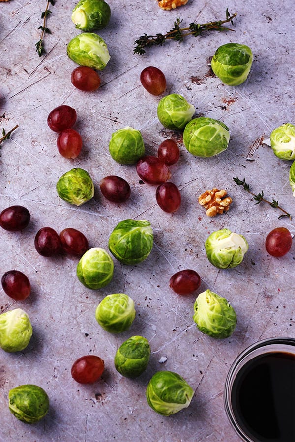 Fresh Brussels sprouts with red grapes, walnuts and fresh thyme with small bowl of Balsamic vinegar on stone.
