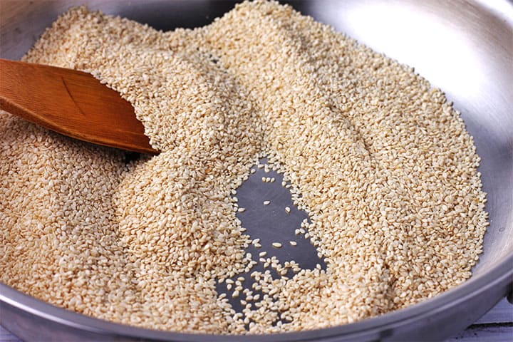 sesame seeds are toasted in stainless steel pan with wooden spoon.