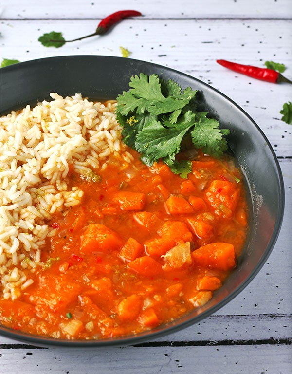 Thai sweet potato curry with rice in black bowl.