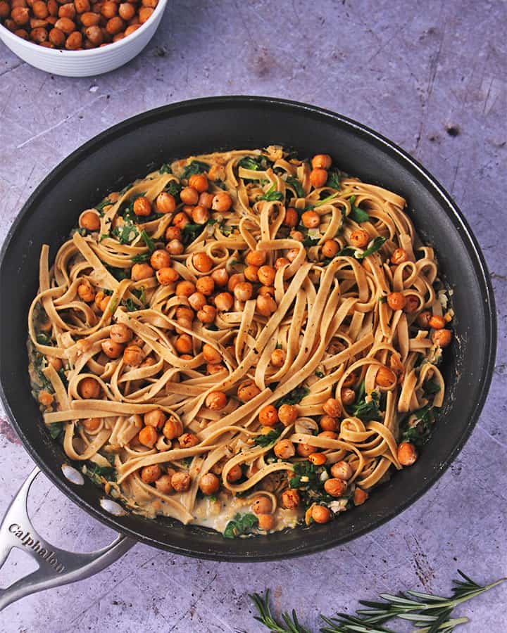 Overhead shot of chickpea pasta sauce with rosemary and spinach with tagliatelle in black skillet.