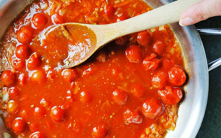 Canned cherry tomatoes are simmered in a pan to make bolognese sauce.