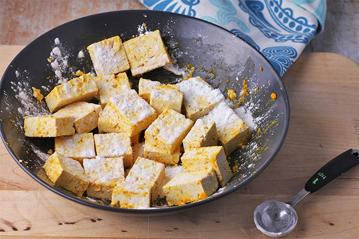 Arrowroot is added to cubes of tofu in black bowl.