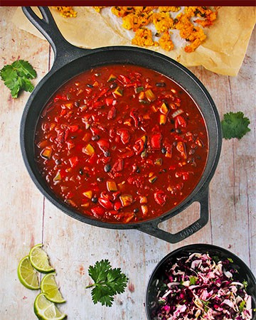 black bean chili in black pan with black dish of cabbage slaw and baked polenta squares