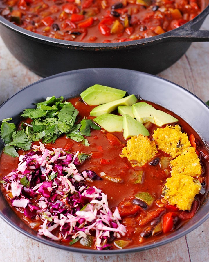 Bowl of black bean chili with cocoa powder topped with jalapeno polenta squares, cabbage slaw, chopped cilantro and avocado cubes