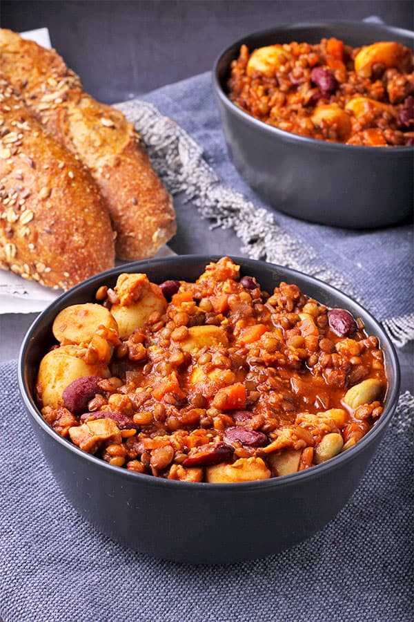 loaded tempeh stew with lentils, beans, potatoes and tomato sauce in black bowl with bread