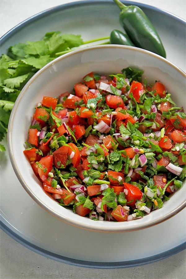 DIY pico de gallo in bowl on plate with jalapeno and coriander.