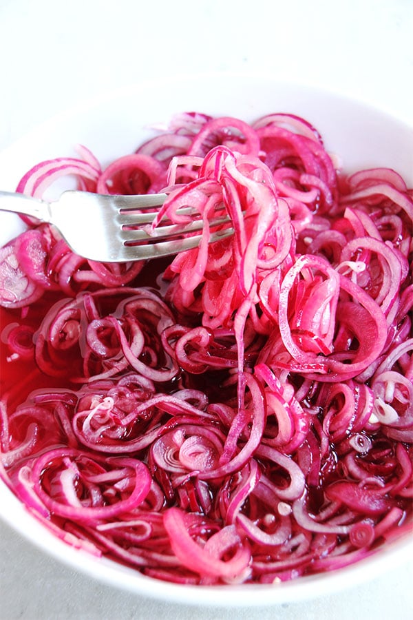 Quick pickled onion slices in white bowl being lifted with a fork