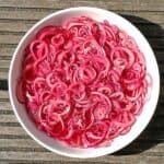pickled red onion slices in white bowl after being marinated are bright pink.