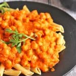 Romesco sauce with chickpeas and pasta on black plate with arugula as a garnish.