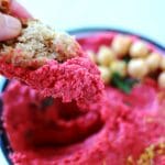 dipping bread into bowl of red spicy beetroot (oil free) hummus.