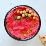 overhead view of spicy beetroot hummus (oil free) in bowl with chickpeas, lemon zest and chopped mint on top.
