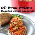 Oil free Briam: roasted veggie casserole on black plate with fork and bread and recipe title in black text in middle of picture.