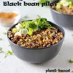 orange quinoa & black bean pilaf in black bowl with orange zest, chopped coriander and sliced green onions on top. Another bowl in background with bowl of Berbere spice blend. Recipe name is on the picture.