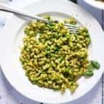 Overhead shot of stovetop mac and peas on white plate with fresh basil and vegan Parmesan on white plate.